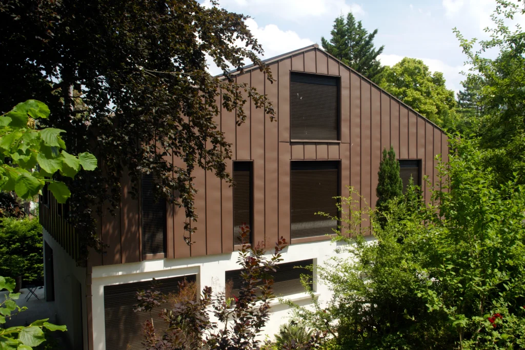 Maison moderne à bardage en métal brun, entourée de végétation.