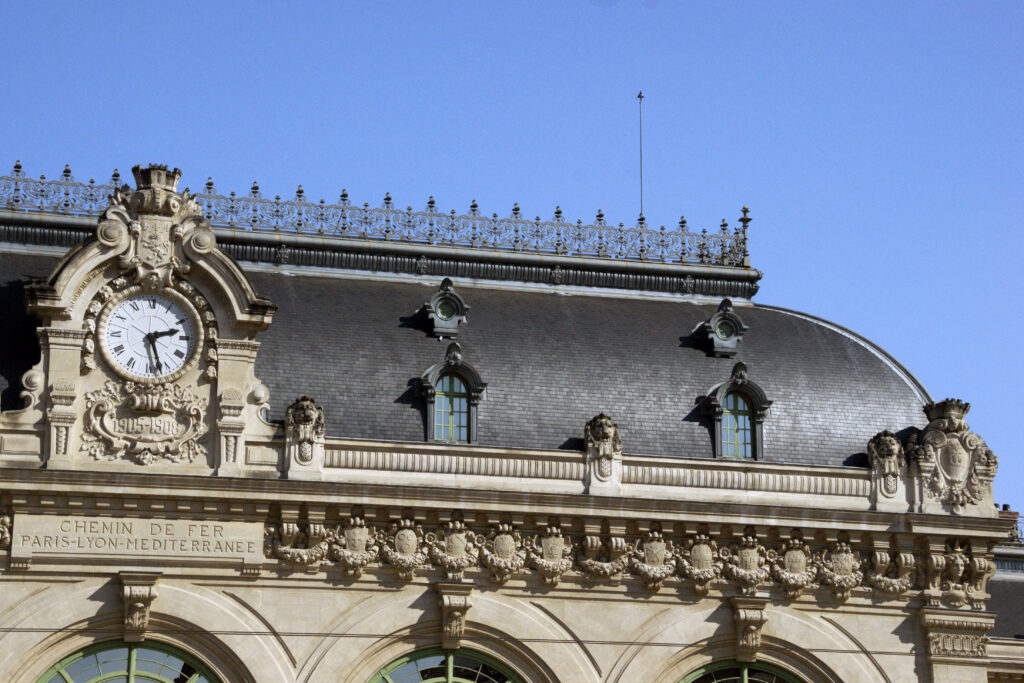 Horloge et ornements architecturaux sous la toiture en ardoises de la gare des Brotteaux.