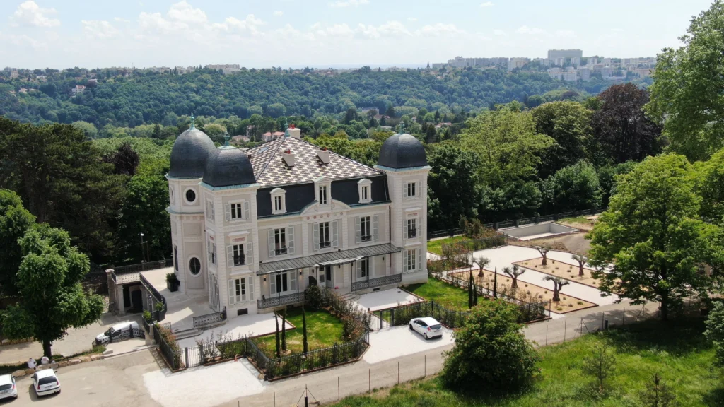 Vue aérienne d'un château entouré de verdure avec toiture en ardoises.