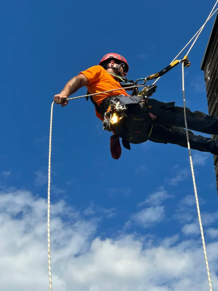 Cordiste suspendu par des cordes, réalisant des travaux en hauteur.