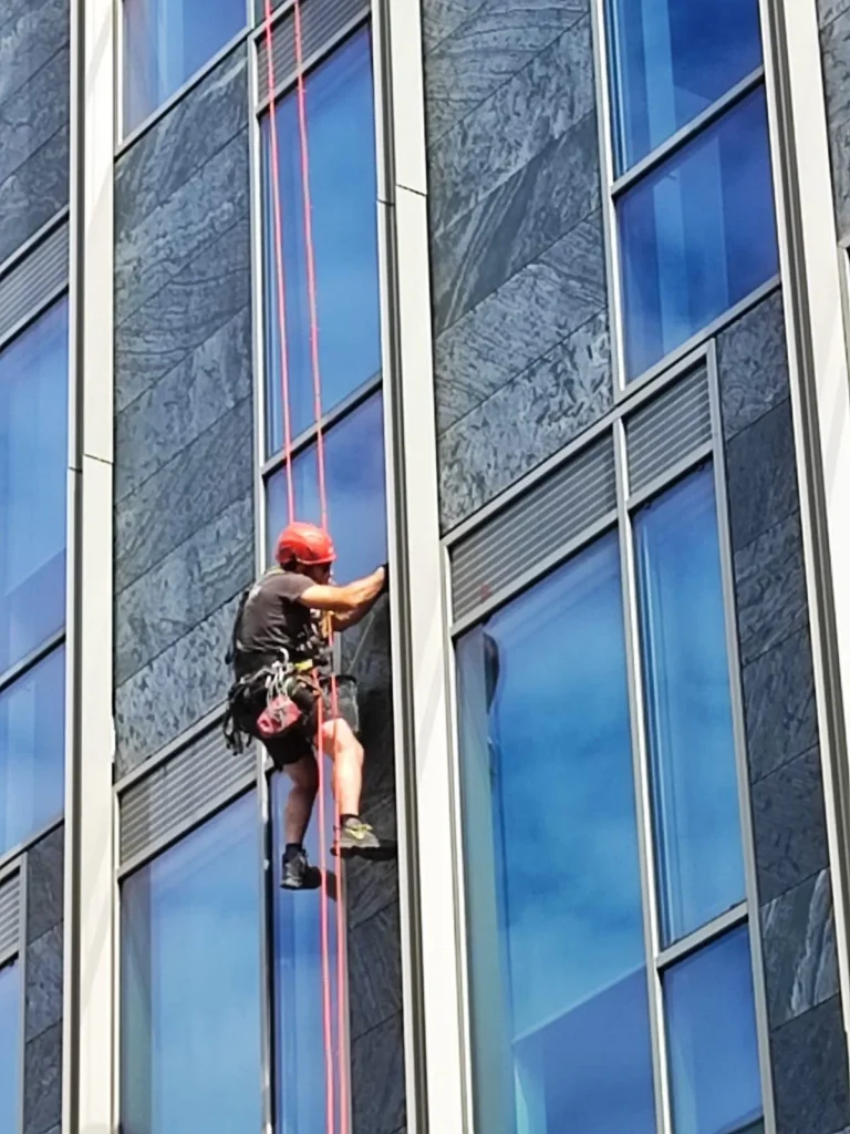 Ouvrier suspendu par des cordes sur la façade en verre d'un immeuble.