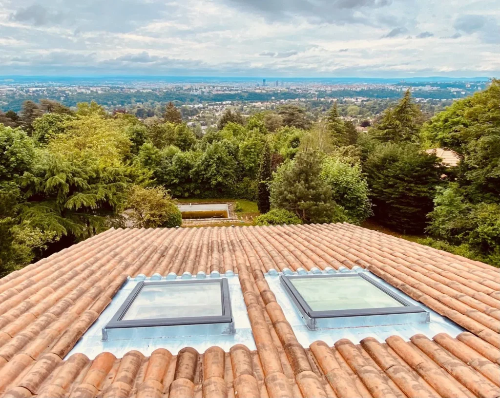 Toiture en tuiles avec fenêtres de toit et vue dégagée sur la ville et la nature environnante.