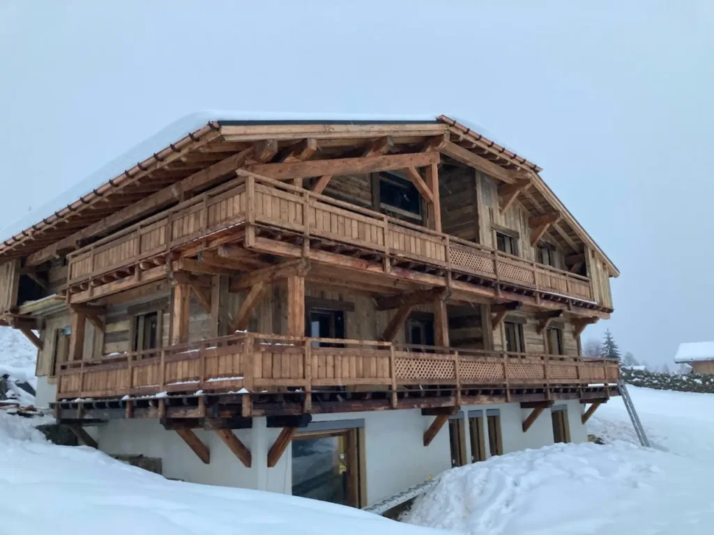 Chalet en bois sous la neige avec balcons en bois sculpté.