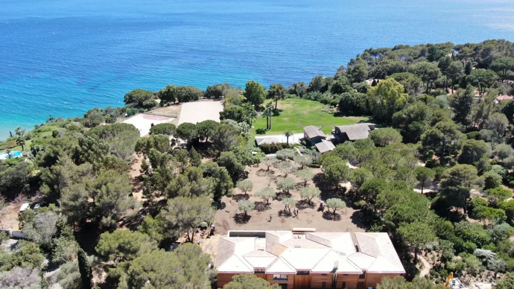 Domaine avec maison en bois, arbres et vue sur la mer.