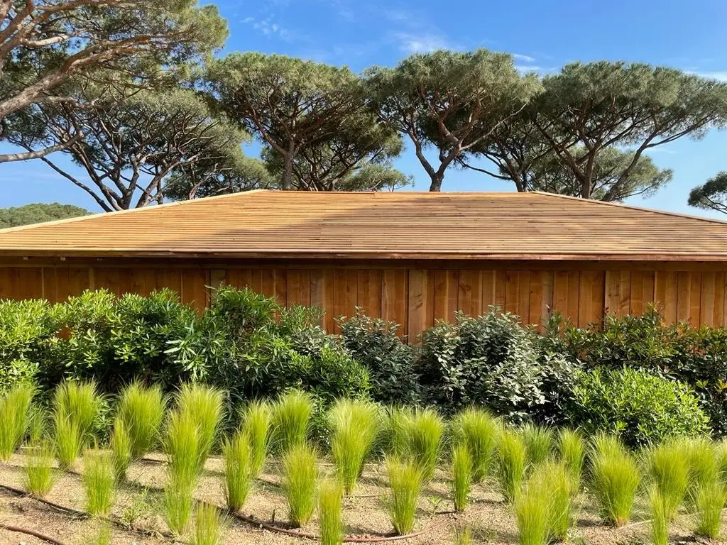 Toiture en bois entourée de verdure et d'arbres sous un ciel bleu.